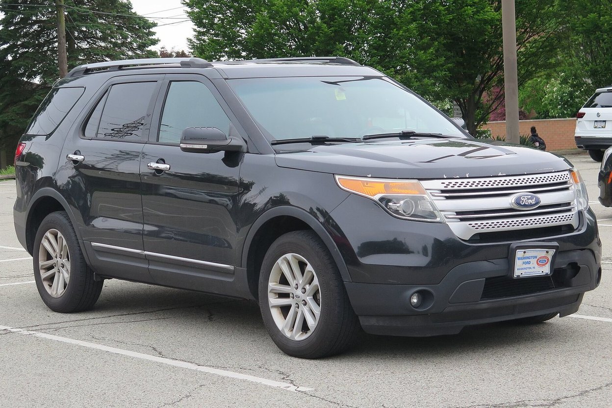 A white fifth-generation Ford Explorer with front-end damage parked in a row at a salvage auction yard, hood slightly buckled