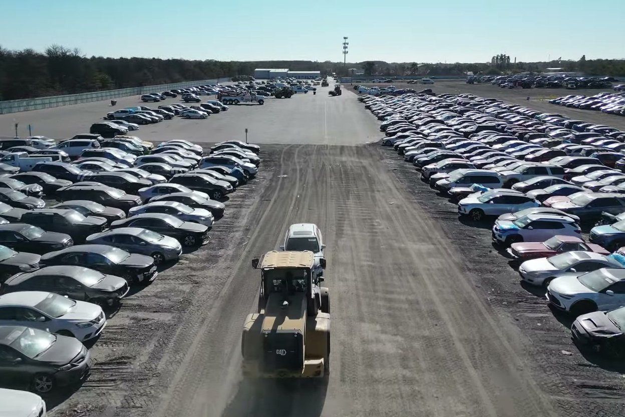 A wheel loader moving a non-running car across a Copart yard, seen from a drone