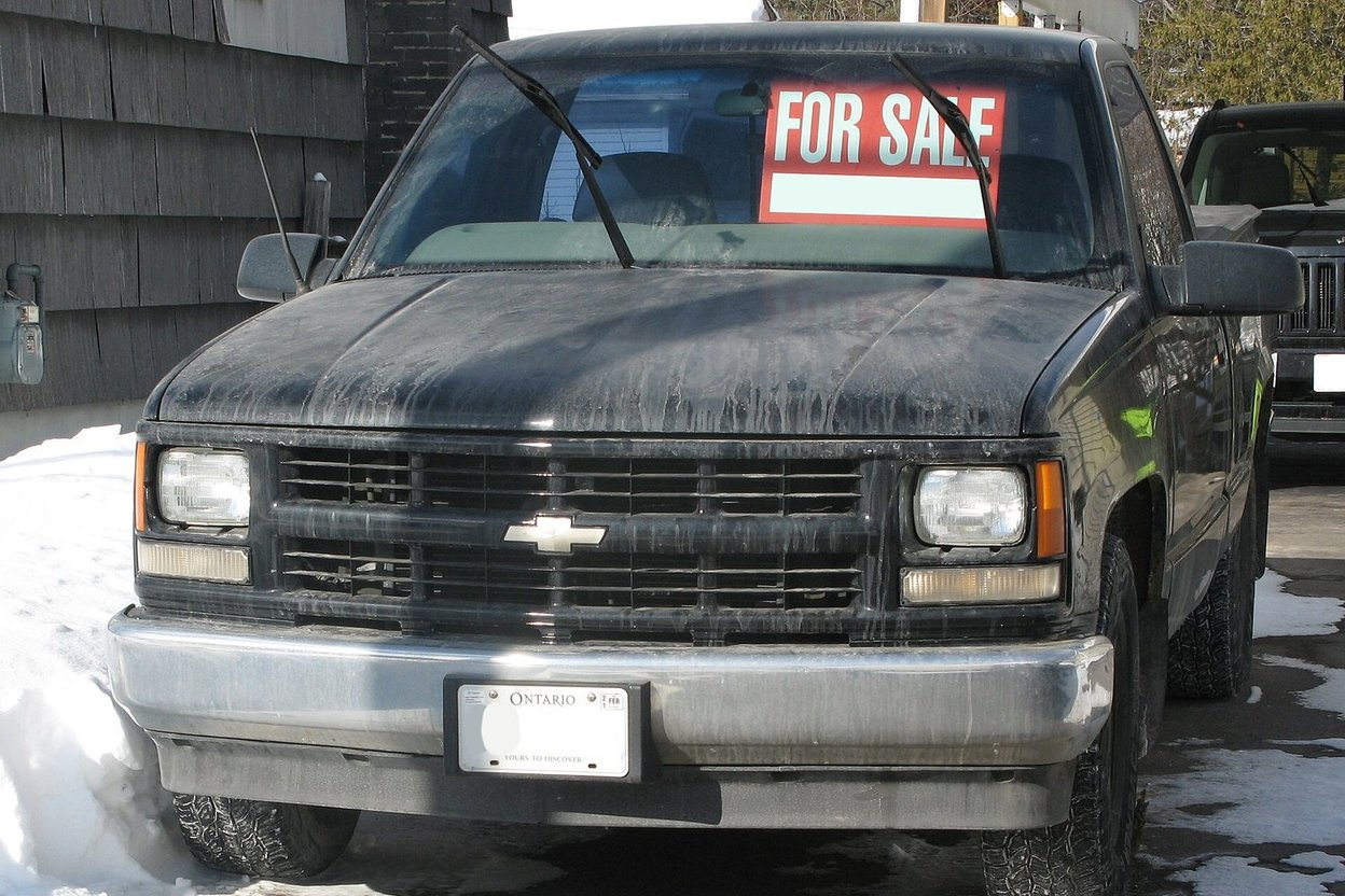 A used pickup truck parked in a driveway with a for-sale sign